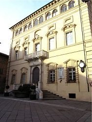 Facciata rinascimentale in pietra chiara con balcone e finestre ad arco, luce solare