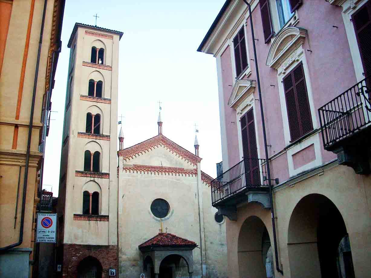 Campanile romanico e facciata della chiesa tra palazzi porticati, luce mattutina