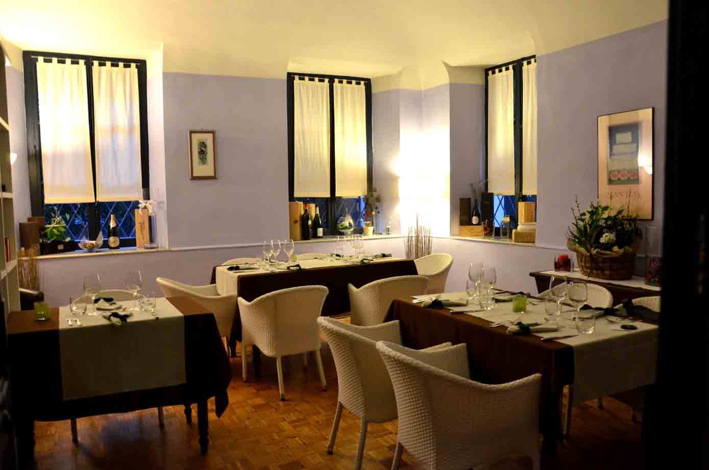 Sala di ristorante con tavole apparecchiate, sedie bianche e finestre con tende chiare