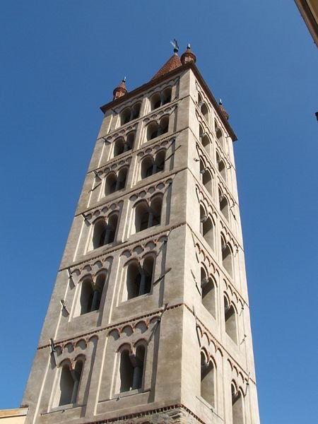 Campanile romanico in pietra chiara con bifore, contro cielo azzurro