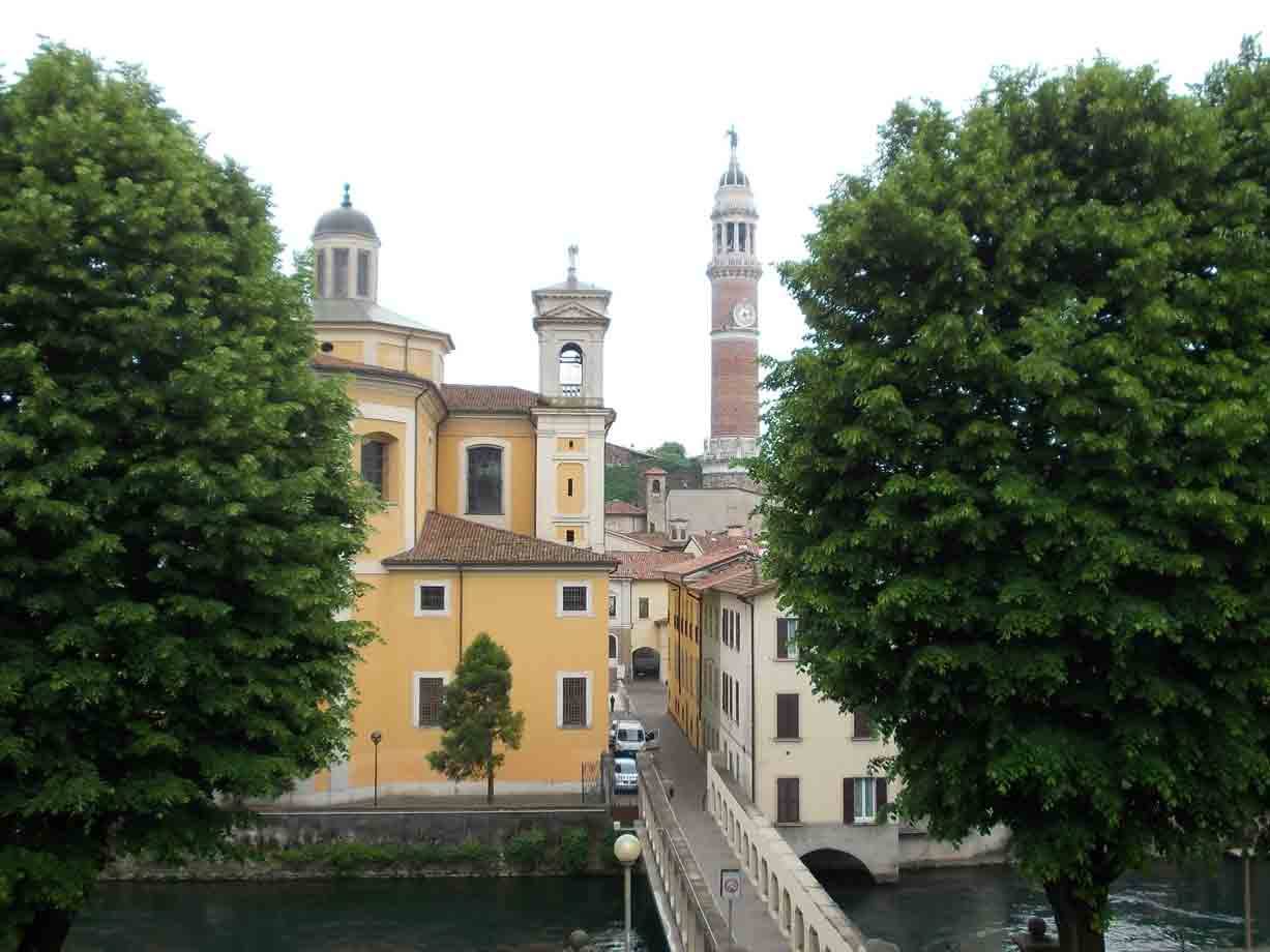 Chiesa gialla e torre civica di Bassano del Grappa tra alberi verdi e ponte