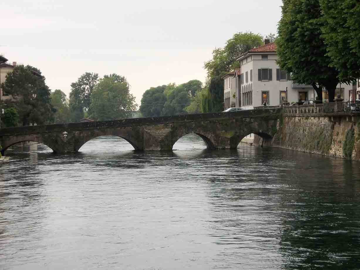 Ponte antico in pietra con archi sul fiume, case affacciate sull'acqua