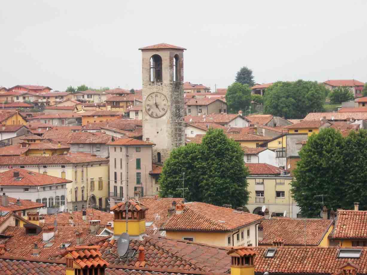 torre civica con orologio sopra tetti di tegole rosse in città lombarda