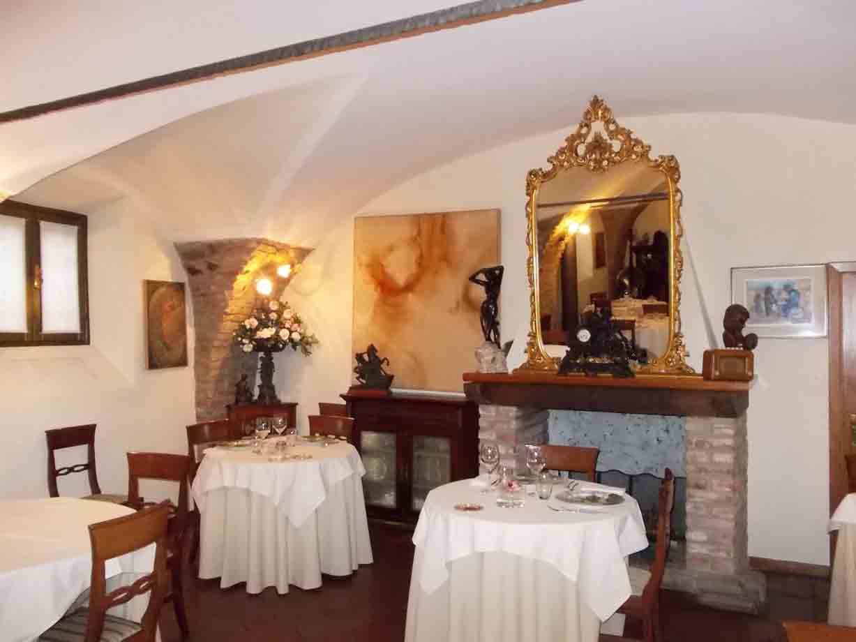 Sala di ristorante con volte bianche, camino in pietra, specchio dorato e tavoli apparecchiati
