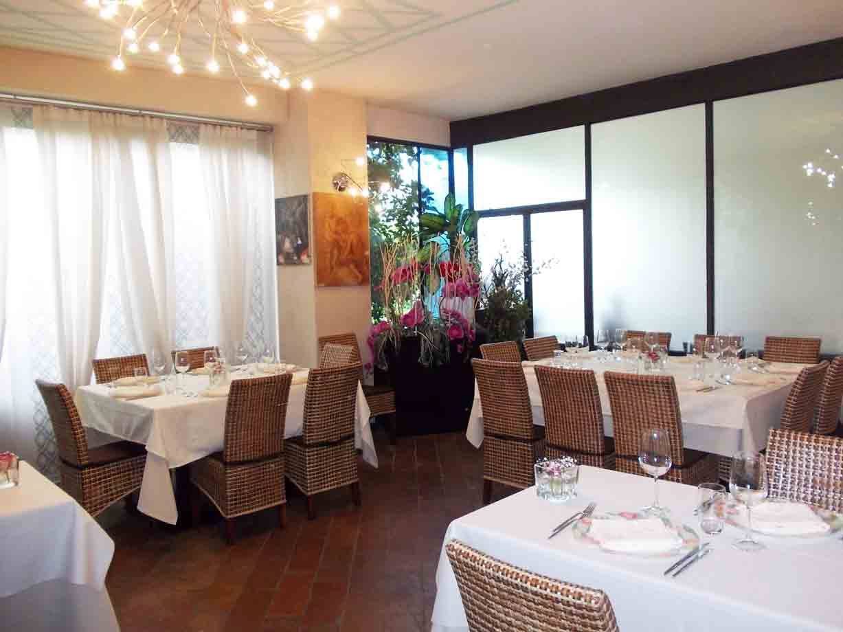 Sala di ristorante con tavoli apparecchiati a tovaglia bianca, sedie di vimini e lampadari moderni