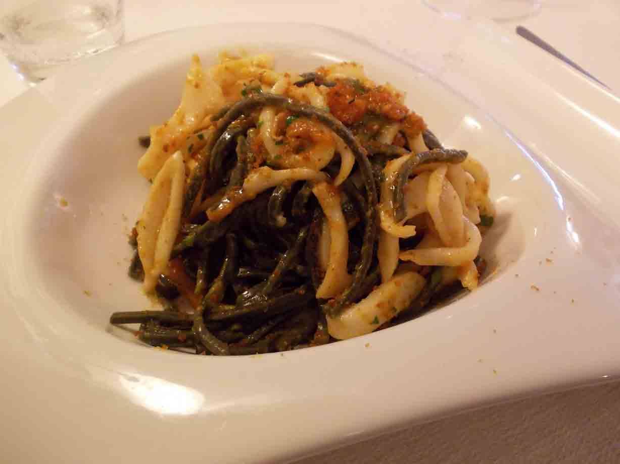 Piatto bianco con pasta al nero di seppia e calamari, luce calda