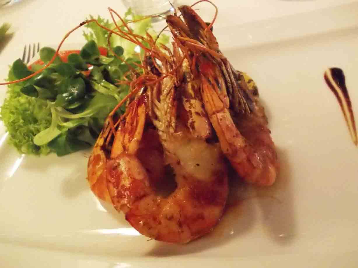 Gamberoni arrosto su piatto bianco con insalata verde e salsa