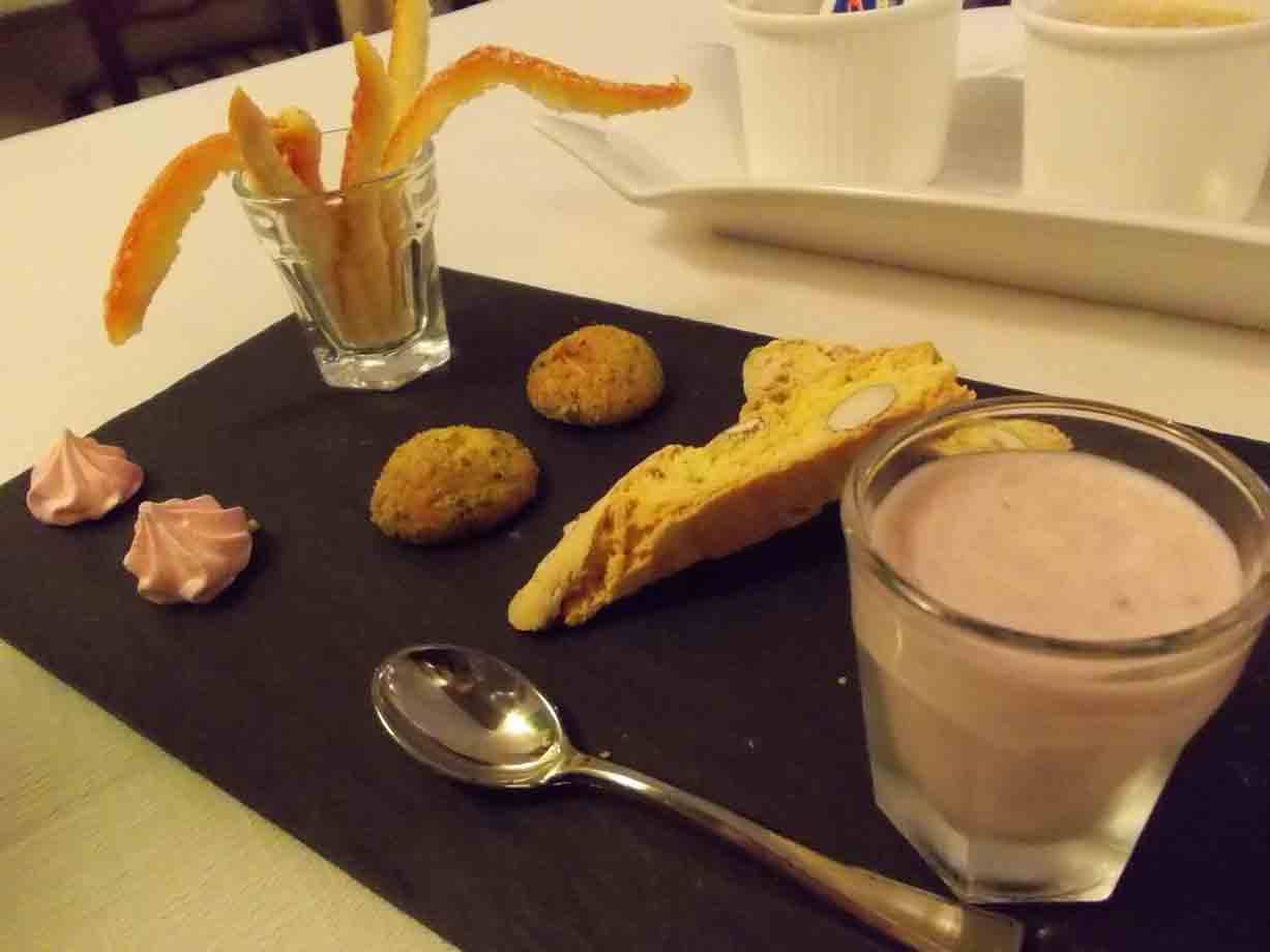 Dolci su ardesia nera: cantuccio, biscotti, meringhe e crema rosa nel bicchiere