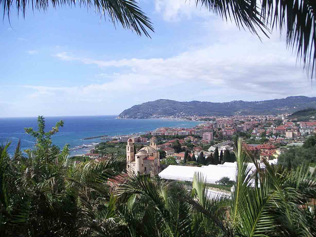 Chiesa con campanile tra le palme sopra il borgo costiero e il mare ligure