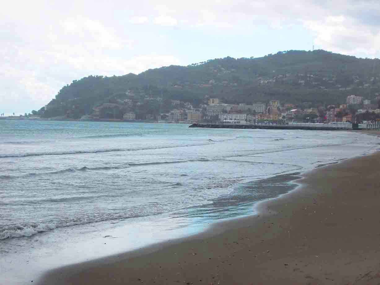 Onde sulla spiaggia sabbiosa, borgo sul molo sotto colline verdi
