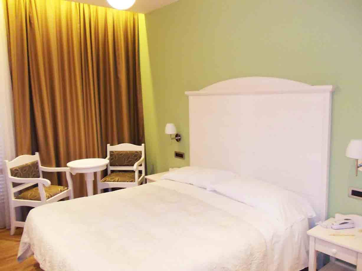 Camera d'albergo con letto bianco, testiera bianca, parete verde e tende oro