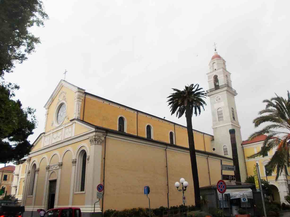 Chiesa gialla con campanile bianco e palme sotto cielo grigio