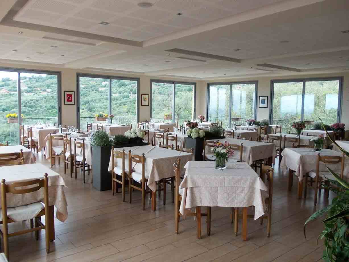 Sala ristorante con tavoli apparecchiati e finestre sui colli verdi