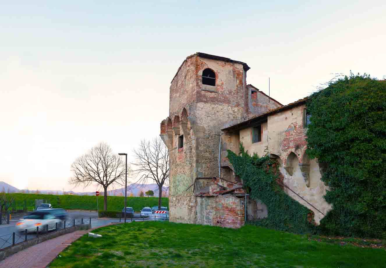Antica torre medievale in pietra con beccatelli, edera e auto in transito