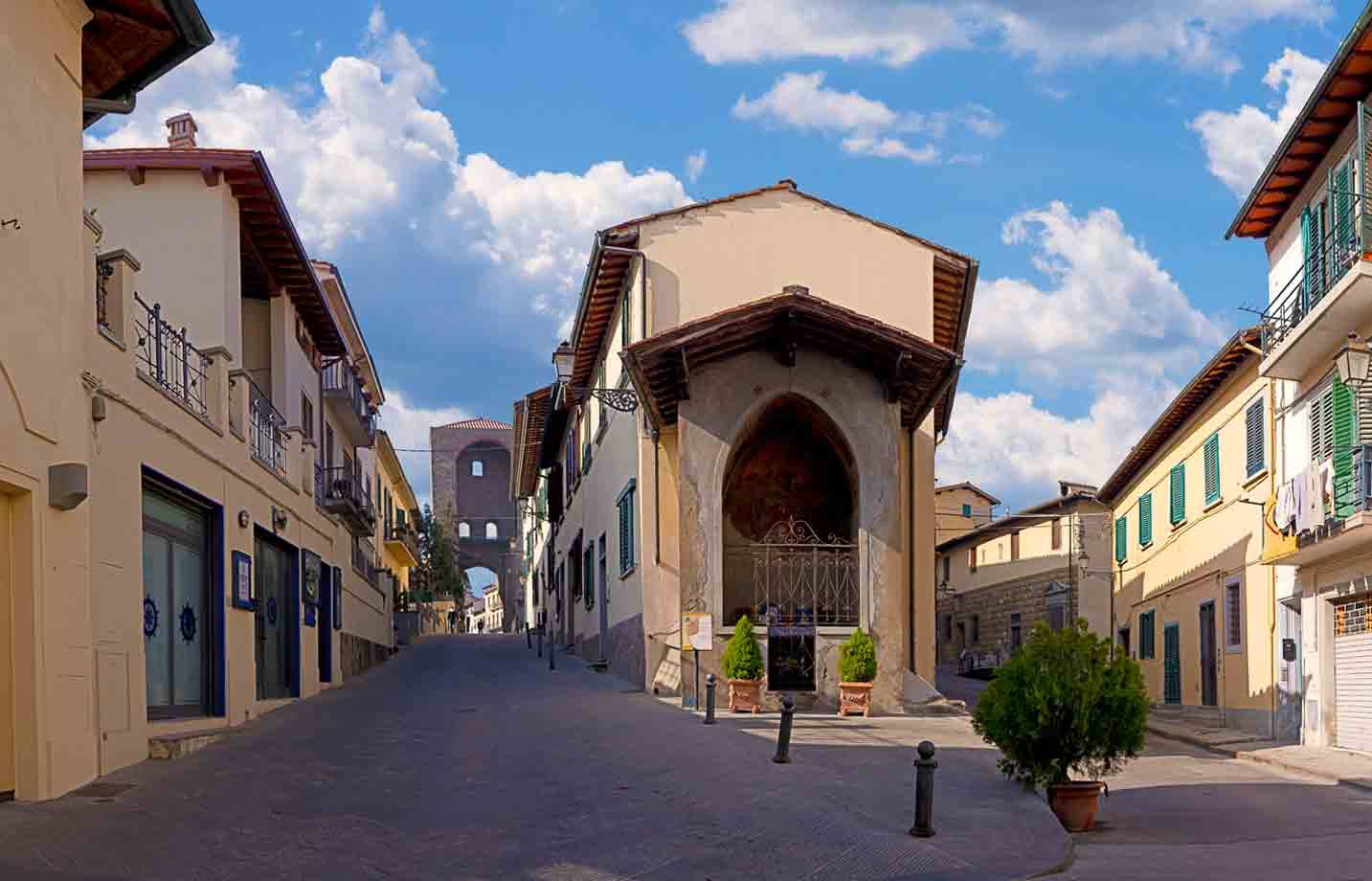 Chiesetta con grande arco aperto su strada lastricata tra case a Lastra a Signa