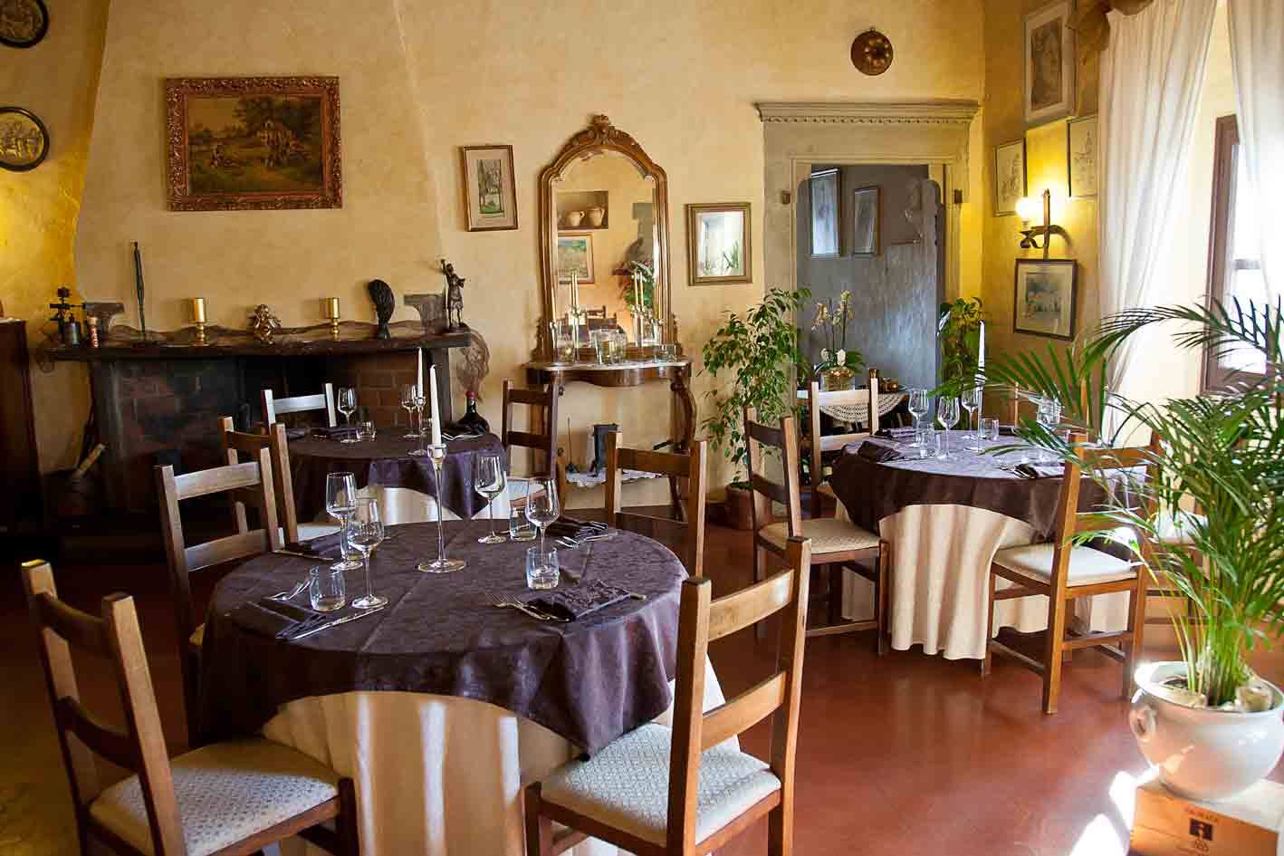Sala di ristorante con tavoli apparecchiati, tovaglie scure, camino, specchio antico e luce naturale