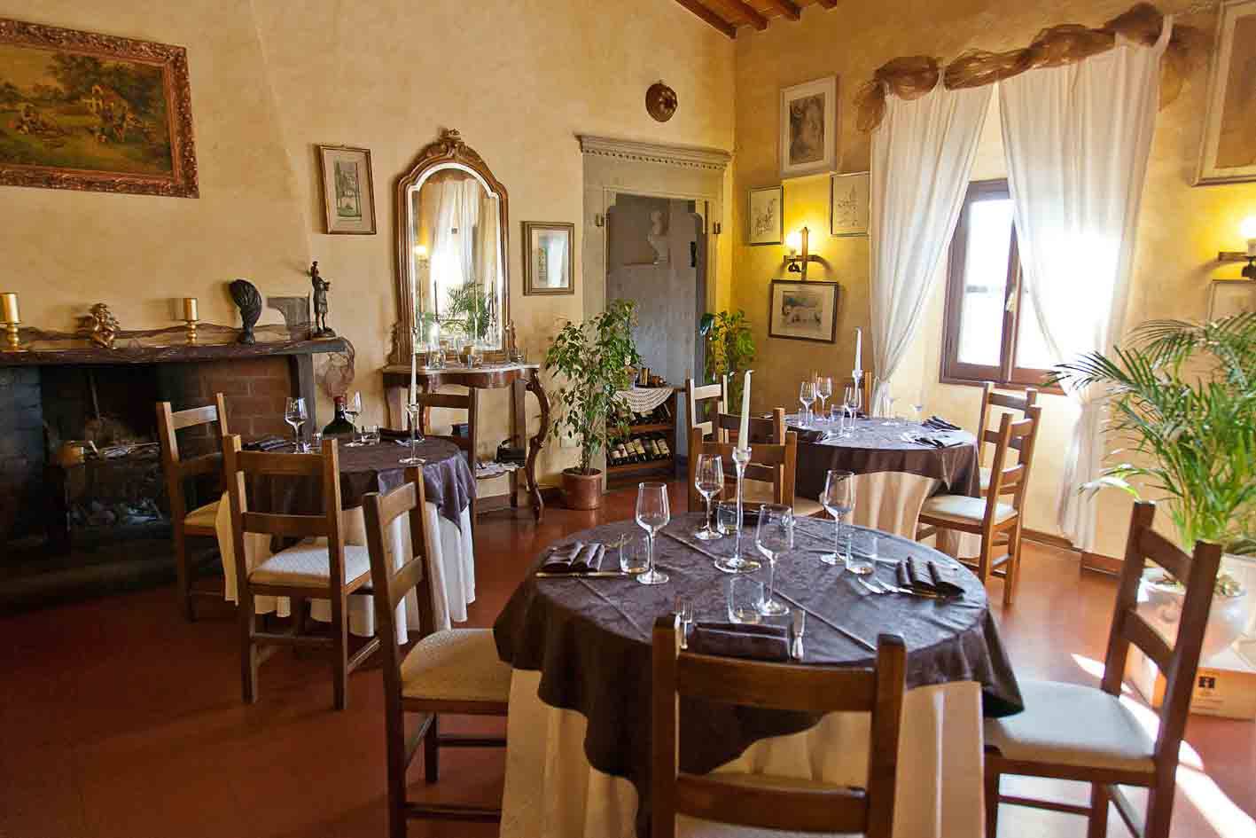 Sala di ristorante rustica con tavole apparecchiate, camino, specchi antichi e luce dalla finestra