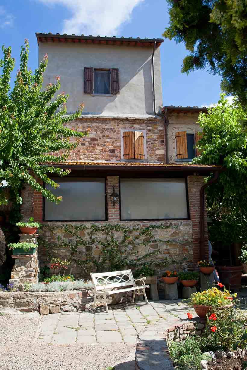 Casa rurale in pietra e mattoni con persiane in legno, panchina bianca nel cortile