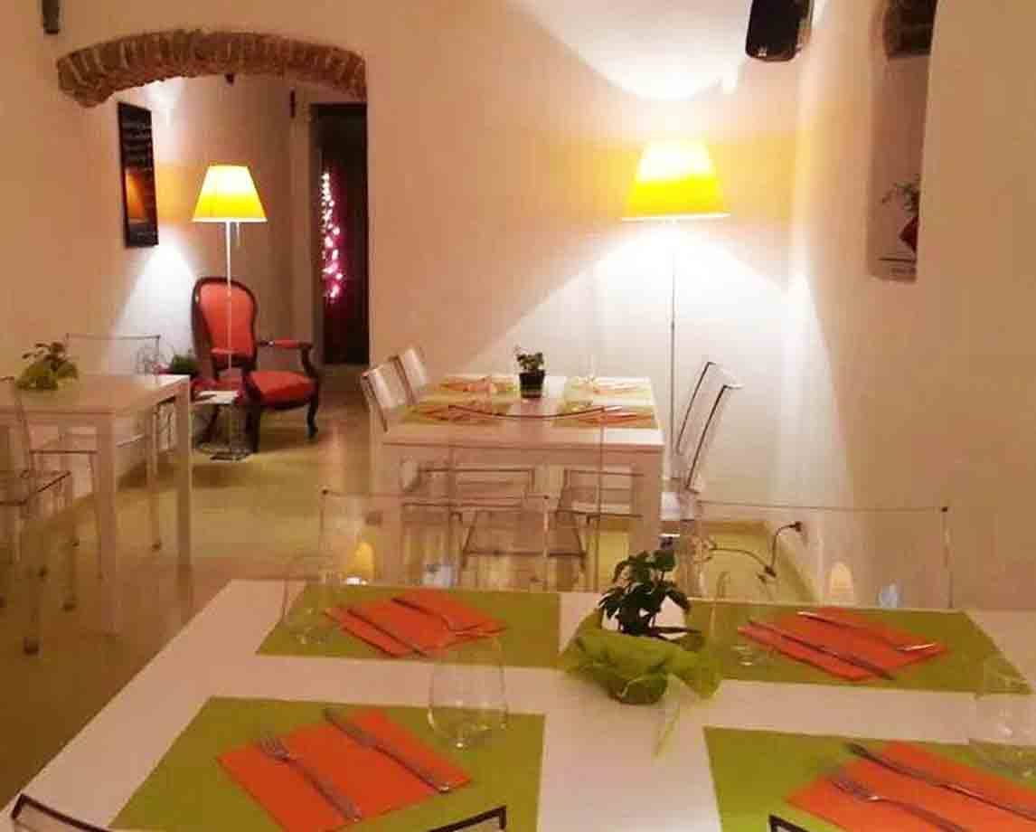 Sala di ristorante con tavoli apparecchiati, tovagliette verdi, poltroncine trasparenti e lampade gialle