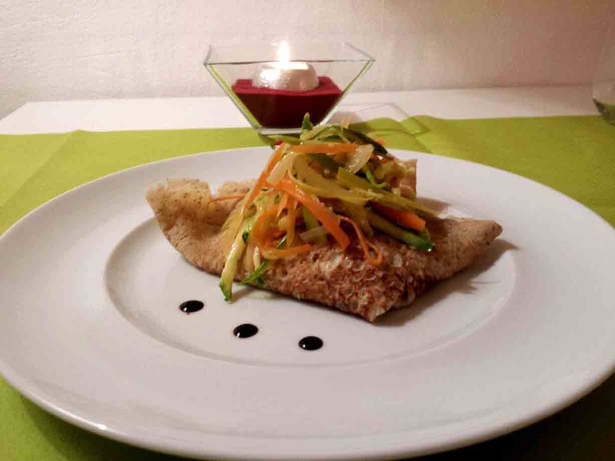 Crêpe di grano saraceno con verdure julienne su piatto bianco, candela accesa