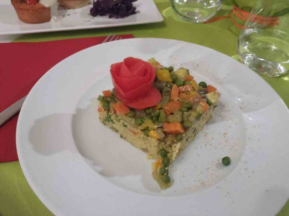 Tortino di verdure con piselli e carote, decorato con rosa di pomodoro, piatto bianco