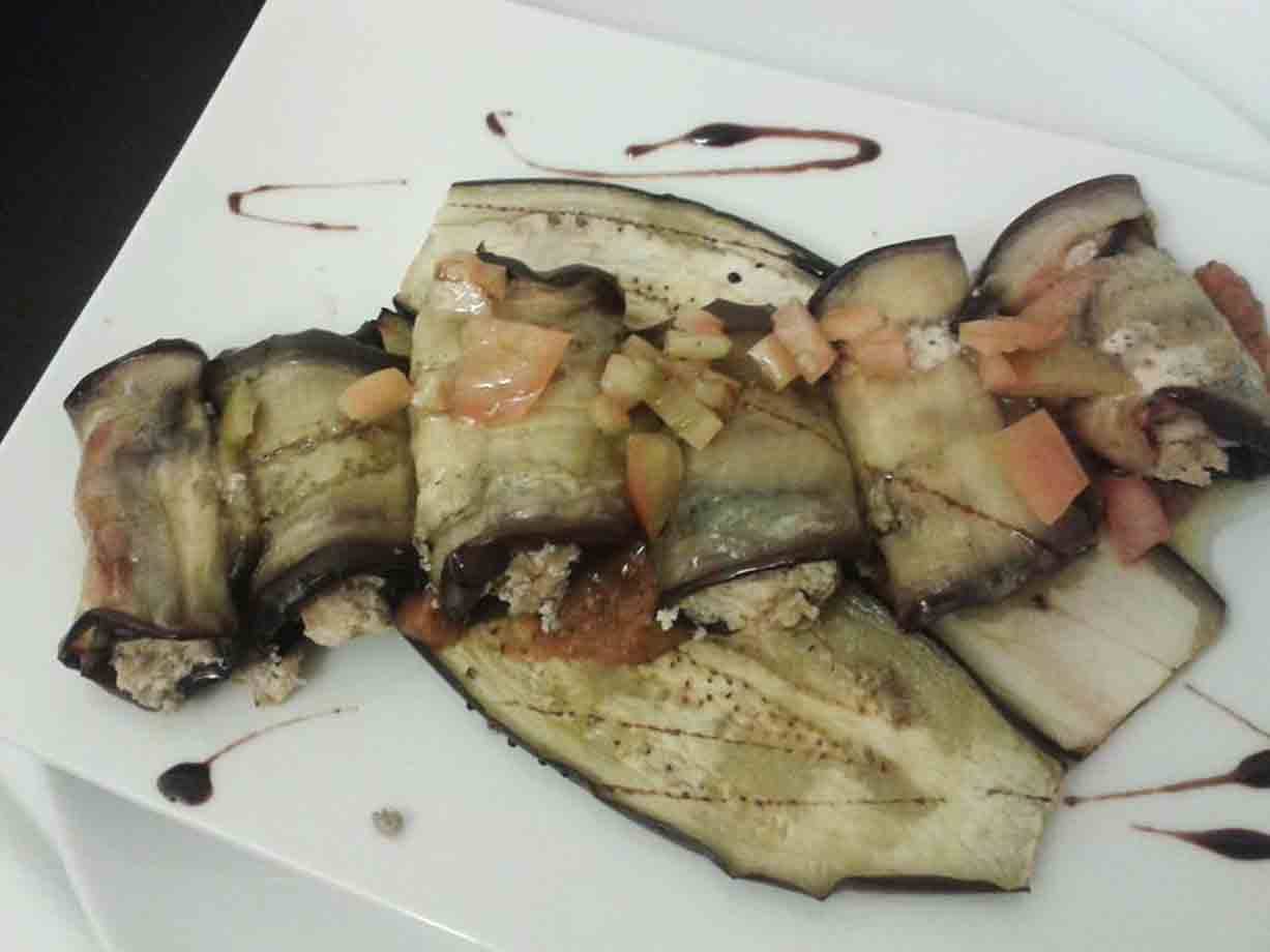 Involtini di melanzana ripieni, decorati con salsa su piatto bianco