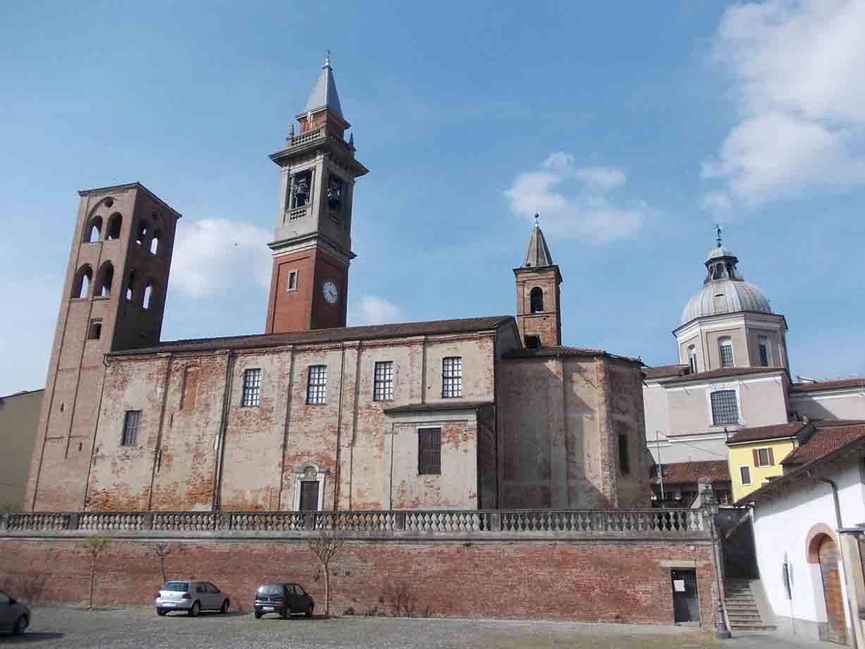 Chiesa in mattoni con campanile e cupola sotto cielo azzurro, auto parcheggiate