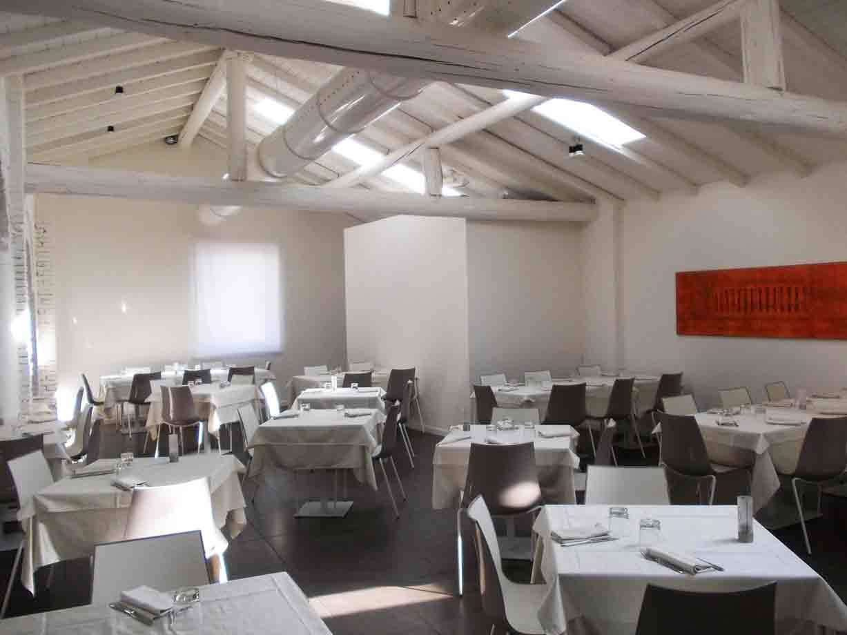 Sala ristorante vuota con tavole apparecchiate, travi bianche e lucernari