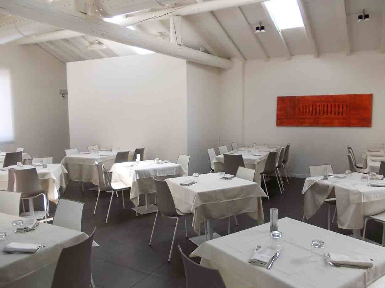 Sala ristorante con tavoli apparecchiati a tovaglia bianca e soffitto con travi