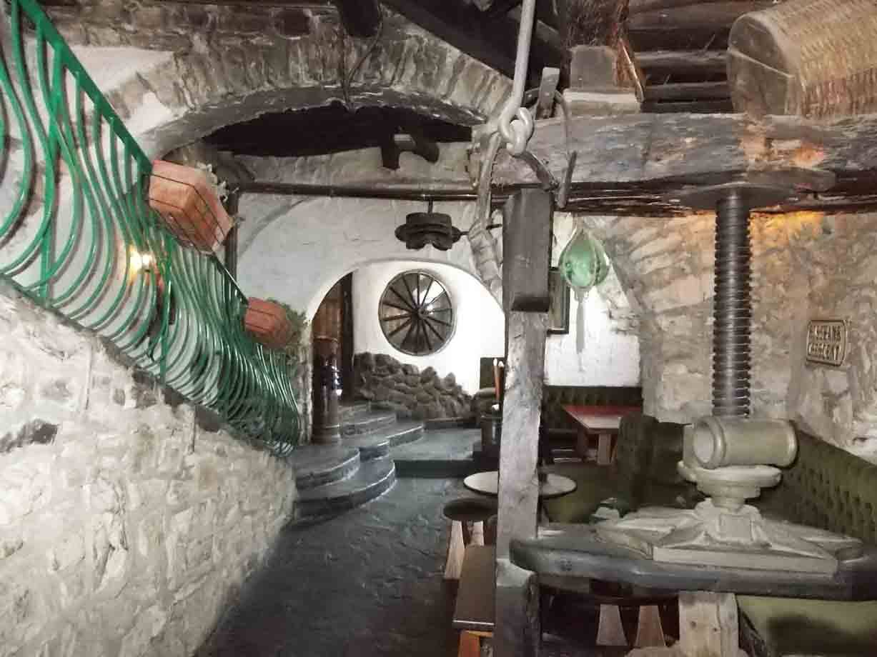Interno in pietra con vecchio torchio a vite, archi e ruota di legno