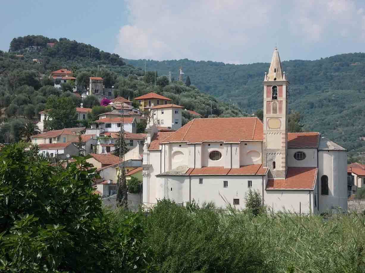 Chiesa bianca con campanile rosa e tetto in coppi tra case e colline