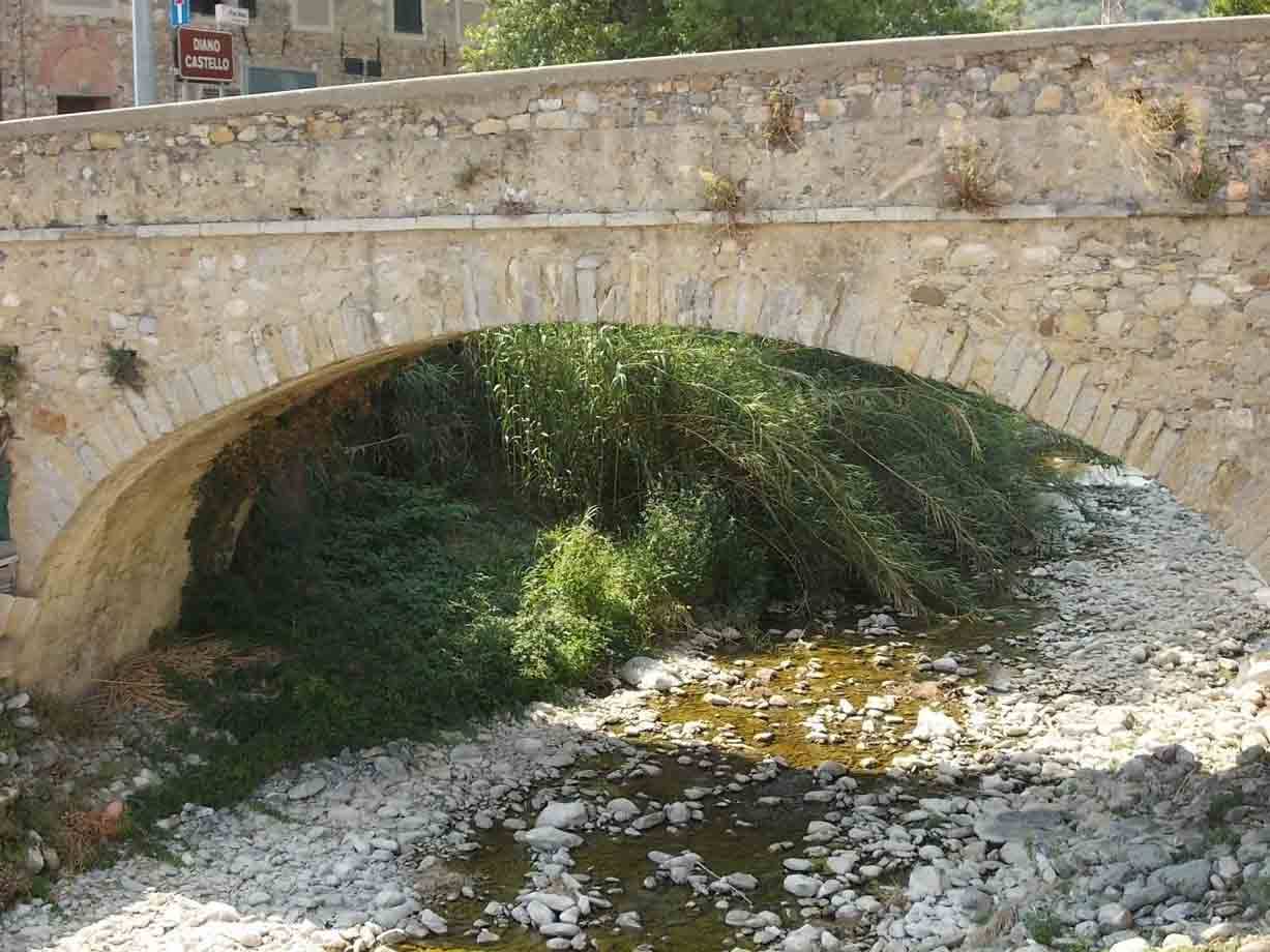 Ponte in pietra a arco sopra un torrente con ciottoli e canneti