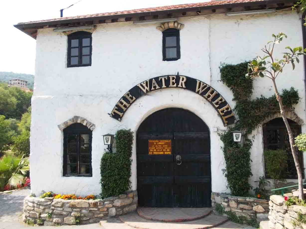 Ingresso arco nero con insegna The Water Wheel su edificio bianco immerso nel verde