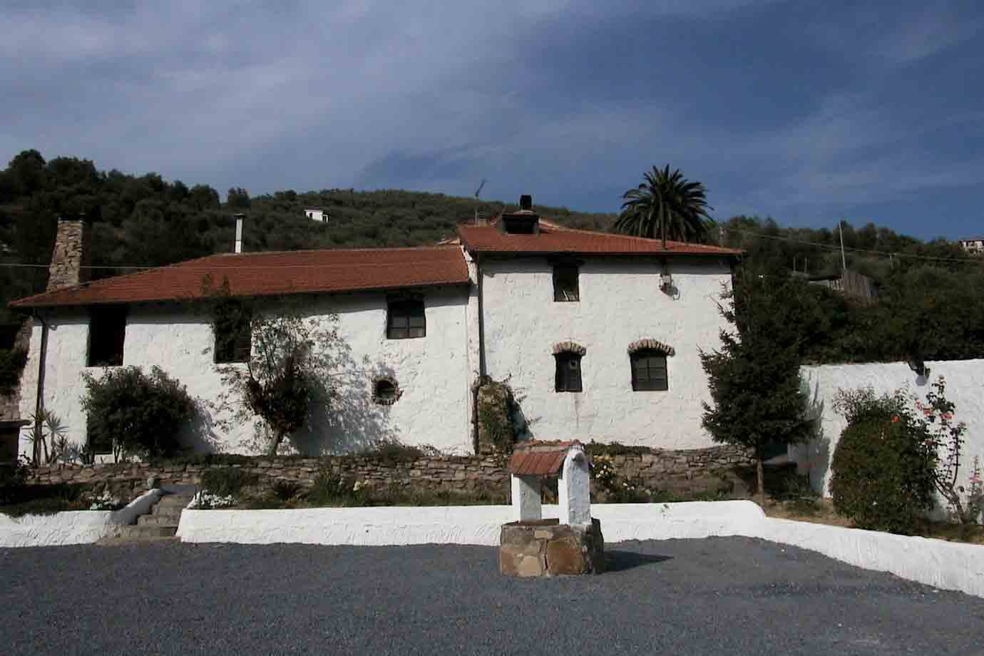 Casa rurale bianca con tetto rosso e pozzo in pietra davanti