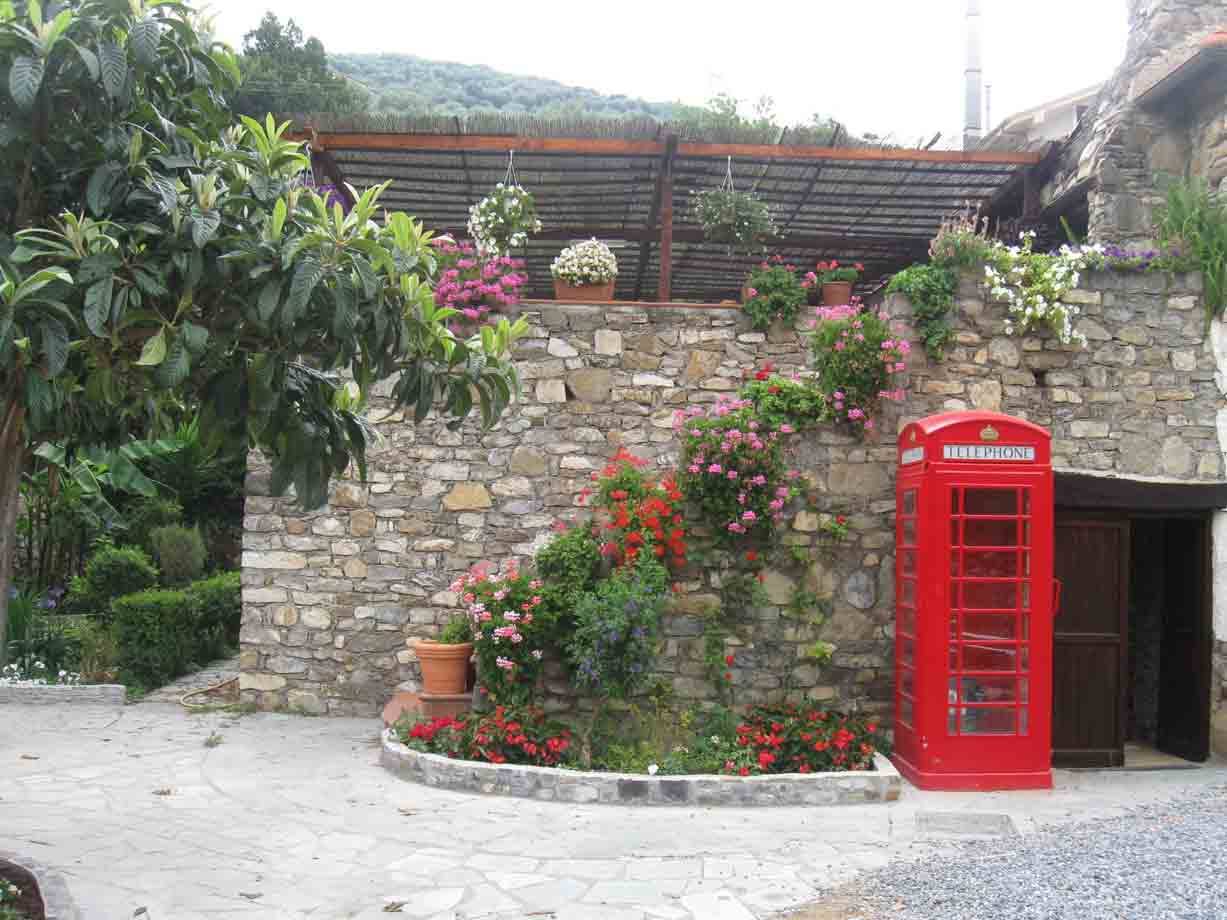 Cabina telefonica rossa contro un muro di pietra con fiori e pergolato