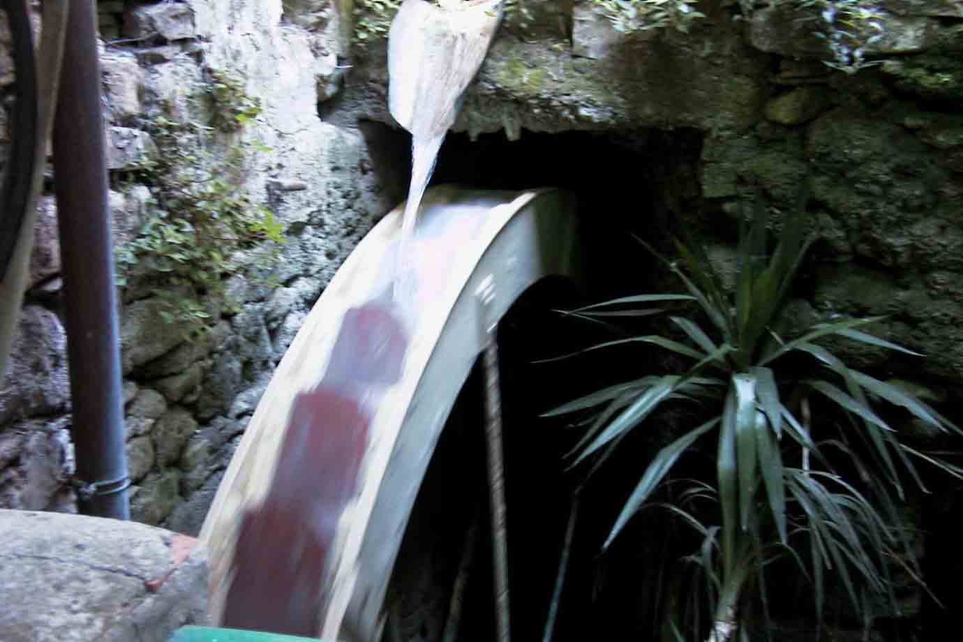 Acqua che scorre su una ruota di mulino in legno tra muri di pietra