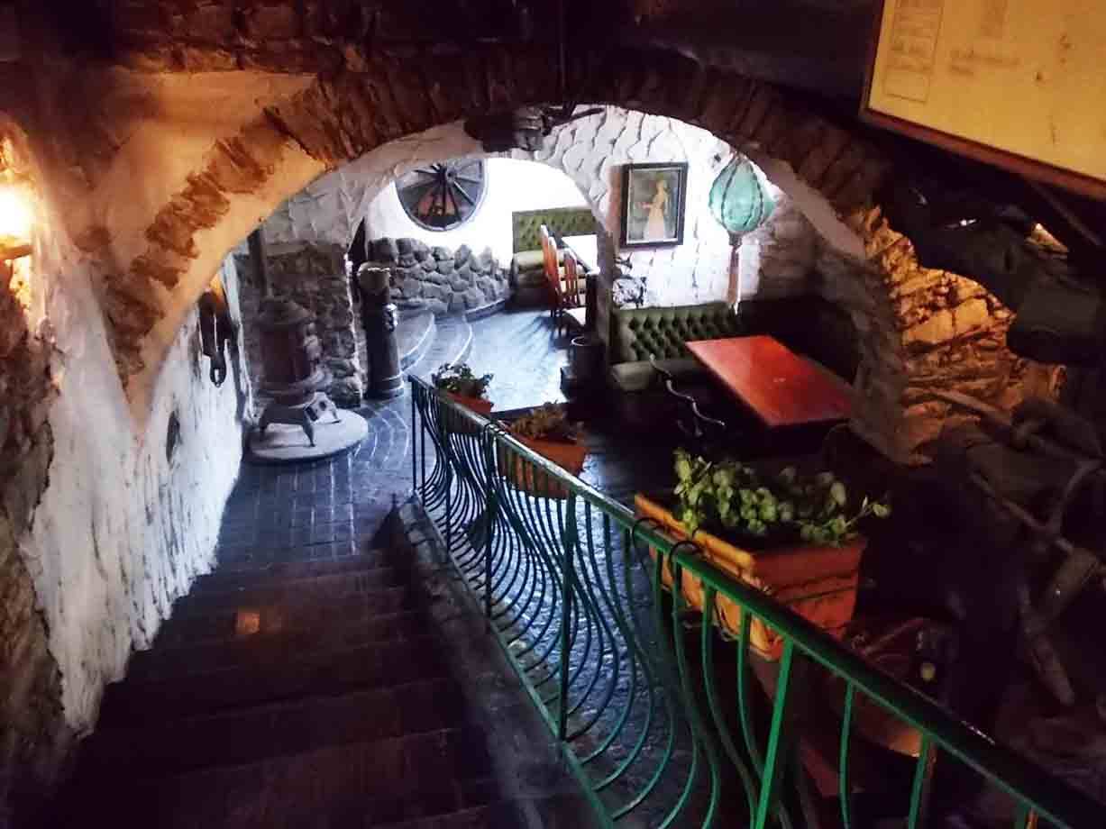 Interno rustico con arco in pietra, stufa a legna, tavoli e ringhiera verde