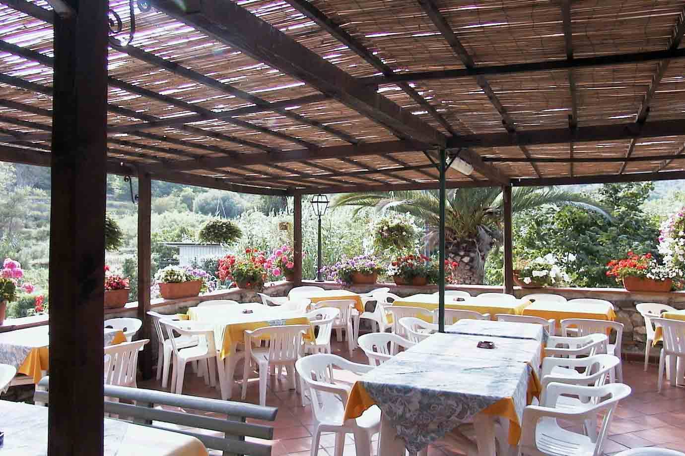 Terrazza coperta di canne con tavoli apparecchiati, sedie bianche e vasi di fiori