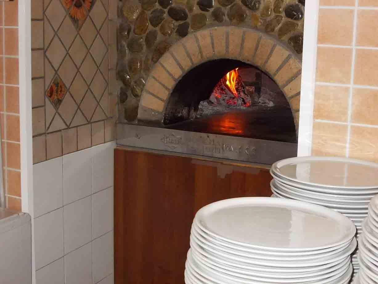 Forno a legna acceso con mattoni e sassi, piatti impilati davanti