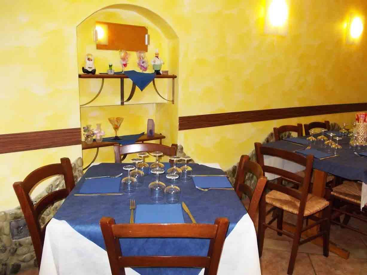 Tavole apparecchiate con tovaglie blu in una sala ristorante dalle pareti gialle