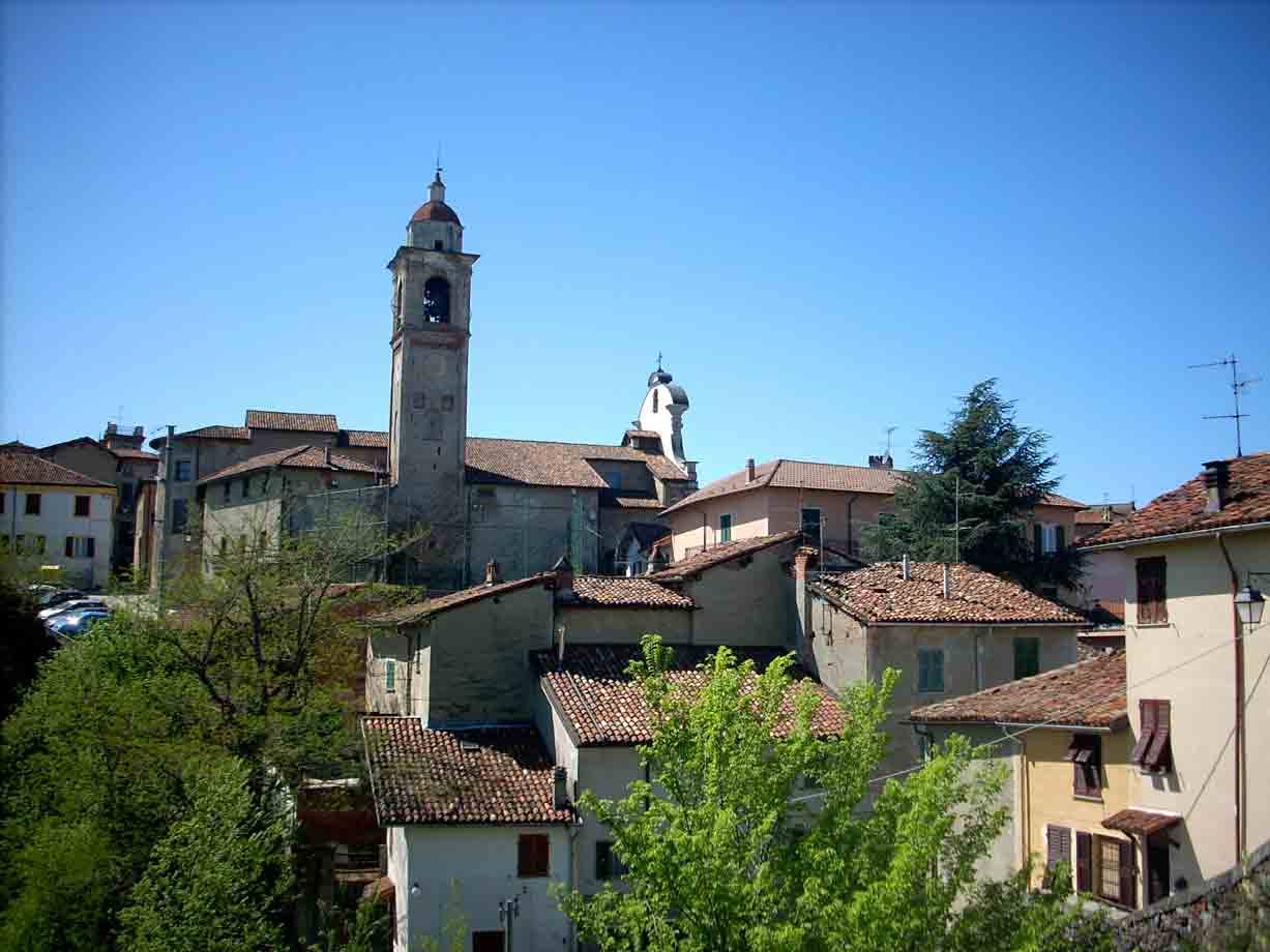 Villaggio collinare con case dai tetti di terracotta e alto campanile sotto cielo azzurro