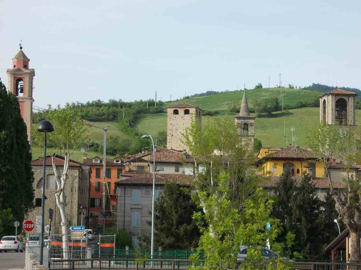 Campanili e torri medievali tra tetti di mattoni, colli verdi sullo sfondo