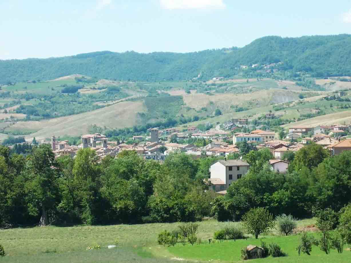 Piccolo borgo con tetti rossi tra colline verdi e boschi