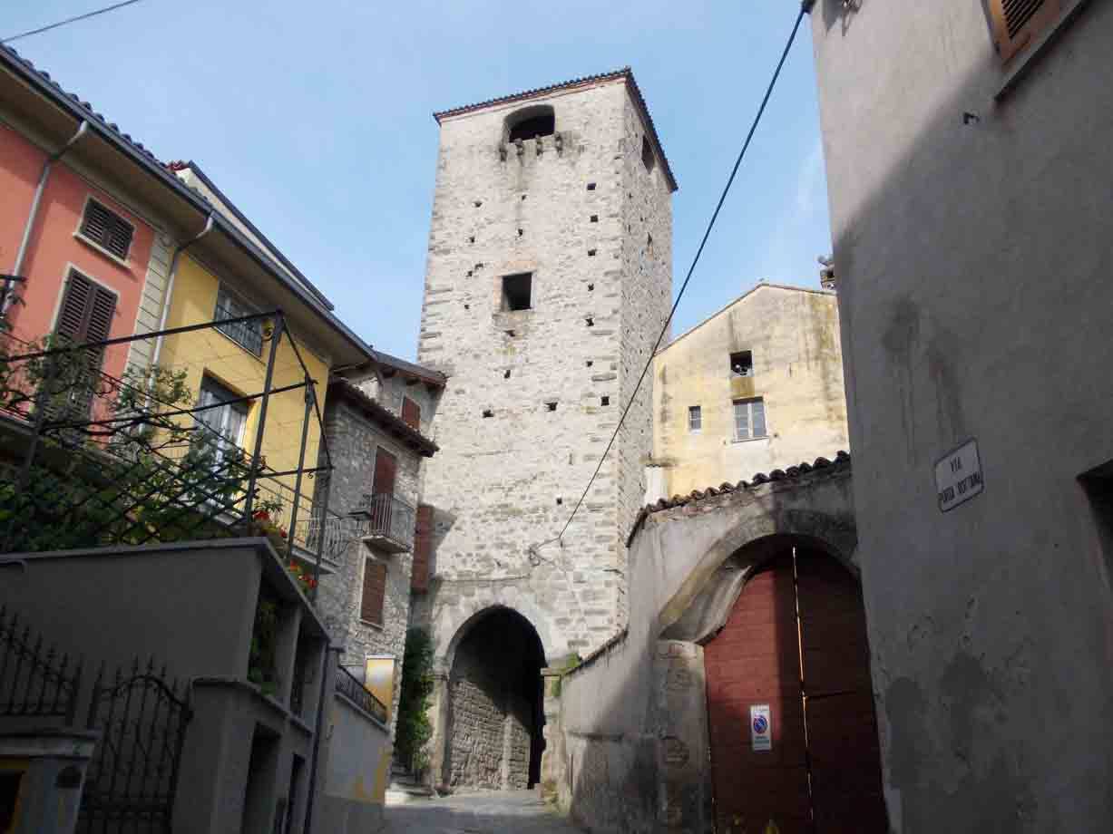 Antica torre medievale in pietra con porta ad arco tra le case del borgo