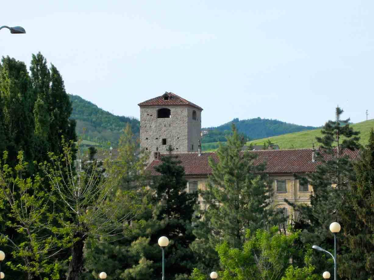 Antica torre in pietra con tetto in coppi sopra edifici tra alberi verdi e colline