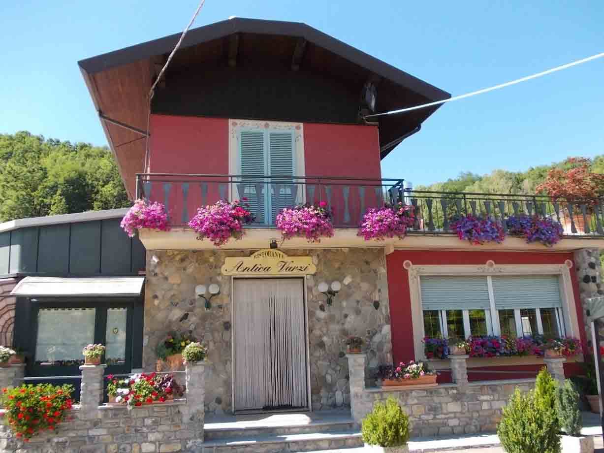 Trattoria Fiori in pietra rossa con gerani rosa sul balcone, colline verdi