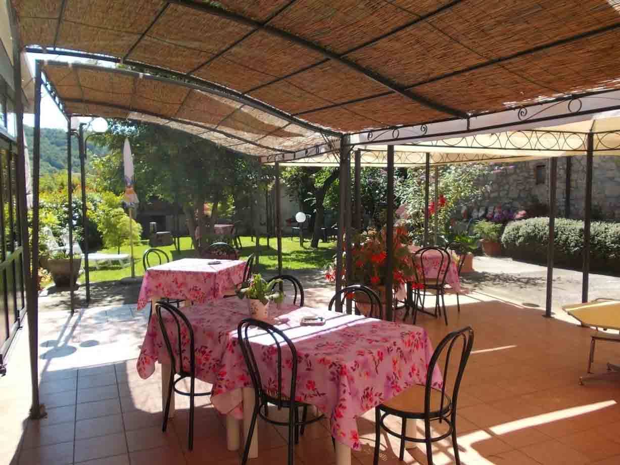 Tavoli con tovaglie rosa sotto pergolato di canne, sedie di ferro nel giardino