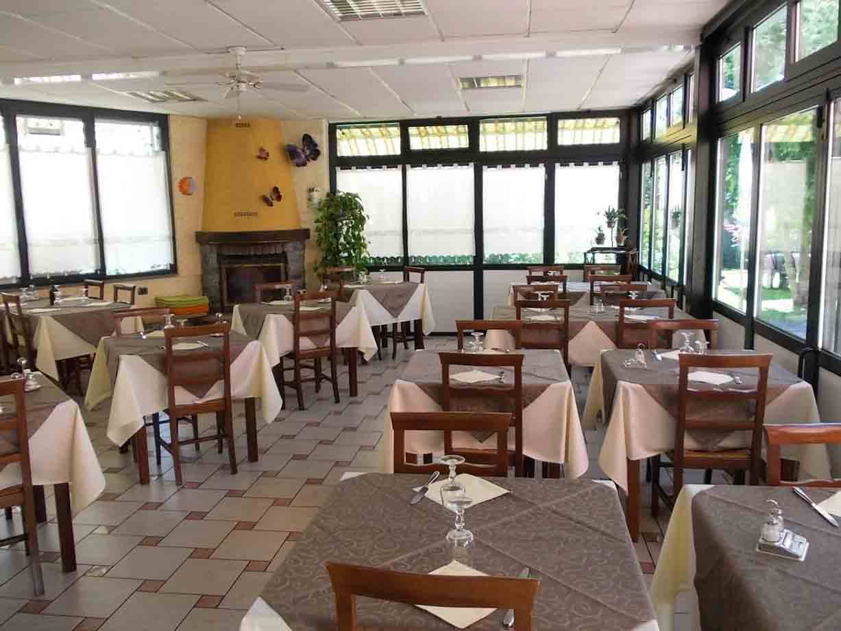 Sala ristorante vuota con tavoli apparecchiati, tovaglie bianche, camino e grandi finestre