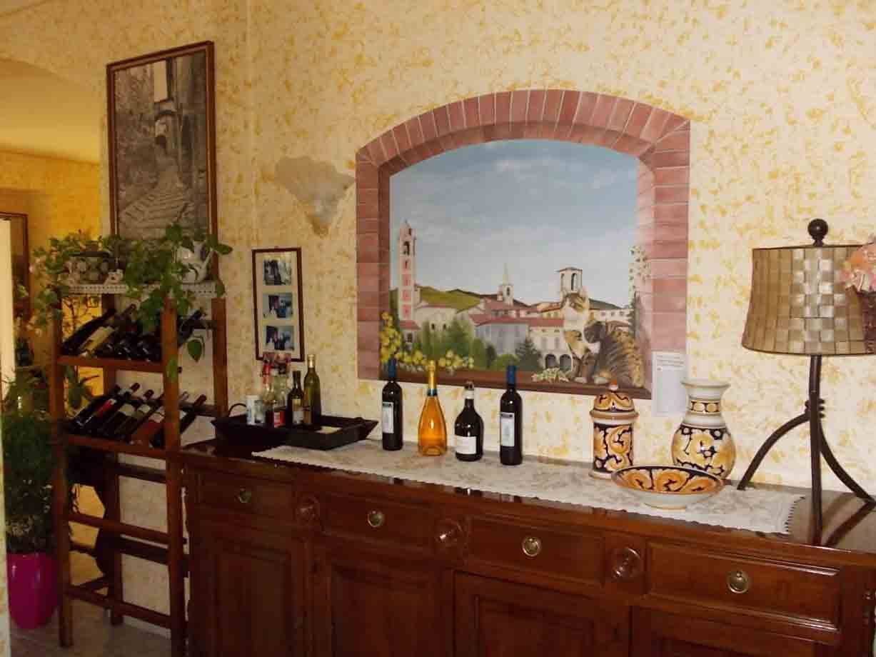 Bottiglie di vino su credenza in legno sotto murales affrescato con arco in mattoni