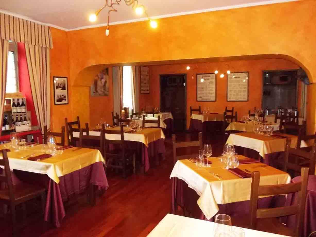 Sala di ristorante con tavoli apparecchiati, tovaglie gialle, pareti arancioni e luce calda